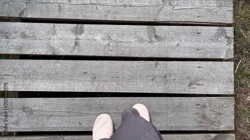 Horizontal video, top view of walking legs in light brown trousers and beige shoes. The feet are walking along a plank path.
