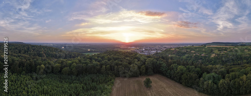 Aerial view of the town of Weingarten nestled among lush forests and agricultural fields during a vibrant sunset with a colorful sky in Weingarten, Baden-Wurttemberg, Germany.