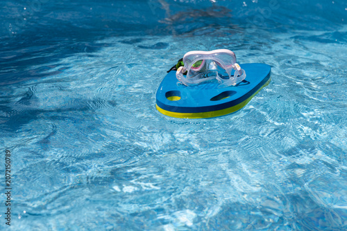 Fotografie Swimming goggles are resting on a floating kickboard on the surface of a swimming pool