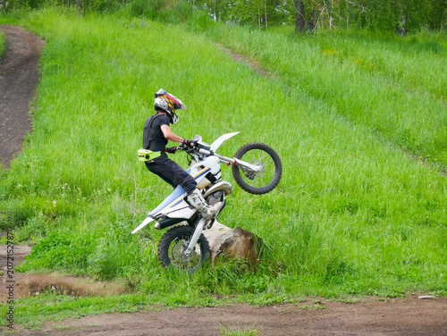 фотографія Motocyclist man performing wheelie on dirt bike across wooden log in grassy field