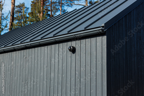 Bild auf Leinwand Charred timber wall with vertical cladding supports a matte metal roof and gutter