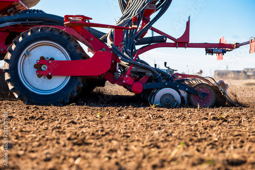 Fotografie A red precision seeder moves across tilled soil, planting uniform rows as dust rises