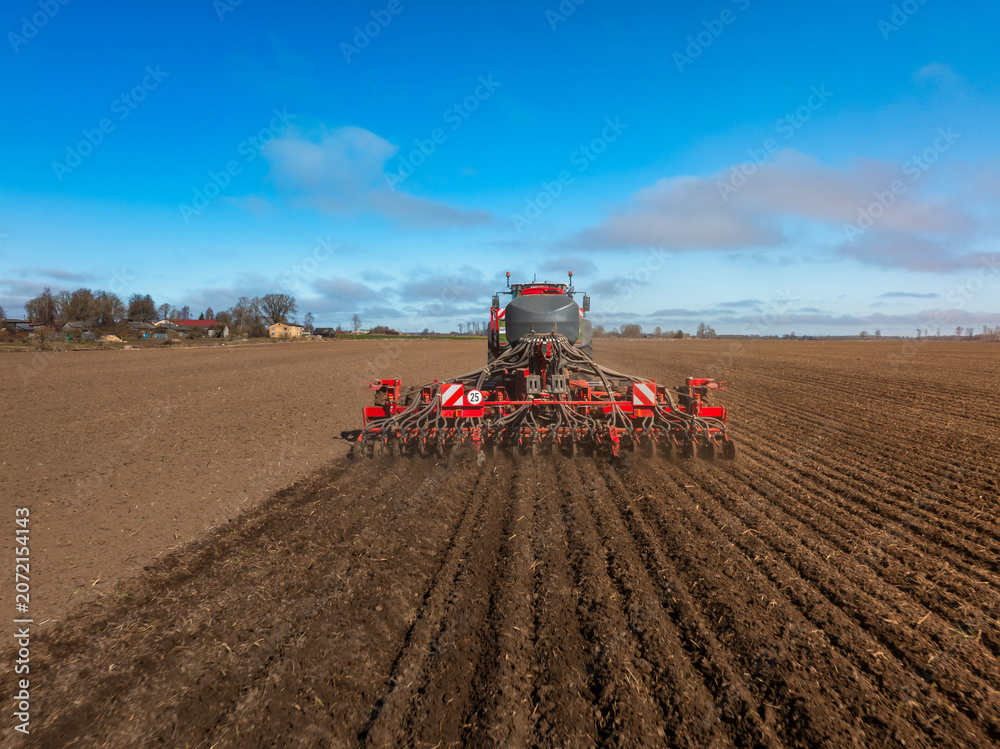 Fototapeta premium Wide angle view shows a tractor towing a seed drill cutting parallel furrows. Seed tubes and coulters are visible. Rural field, cool clear day, strong daylight.