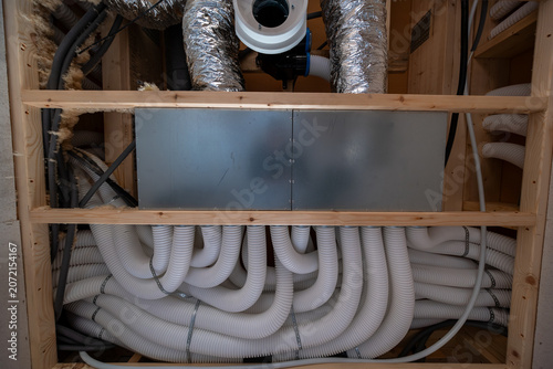 Cuadro en lienzo A framed mechanical closet holds a central metal manifold, foil supply and return ducts, and coiled white ventilation hoses under soft daytime interior lighting