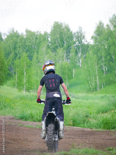 Man motocross rider sitting on motorcycle outdoors. Motocyclist wearing safety gear and helmet riding bike on nature track. Extreme sport and adventure lifestyle, outdoor activity concept.