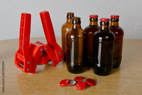 Grupo de botellas de cervezas artesanal, chapadora y chapas rojas sobre mesa de madera