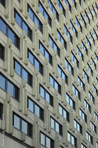 Obraz na plátne Low angle perspective view of a modernist skyscraper concrete exterior featuring a geometric grid of repeating identical windows with blue glass