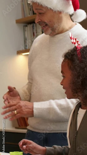 Vertical video: Clapping, dad in Santa hat teaching son making cookies at counter with green cutter