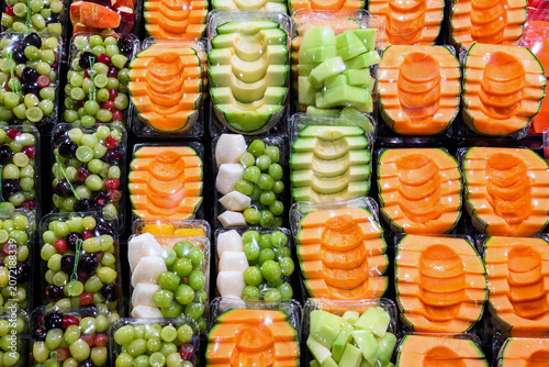 Top view of various pre-cut fresh fruits in plastic containers displayed at a supermarket. Assorted sliced cantaloupe melons and green grapes. Healthy convenience food concept.