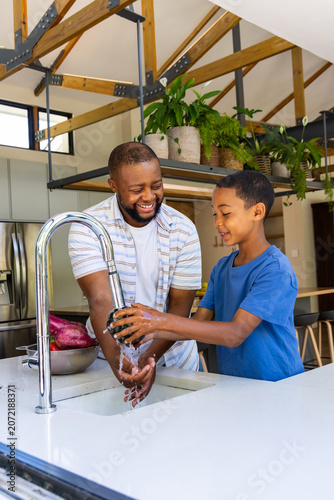 Canvastavla African American father and child rinsing dark fruit under chrome tap at white i