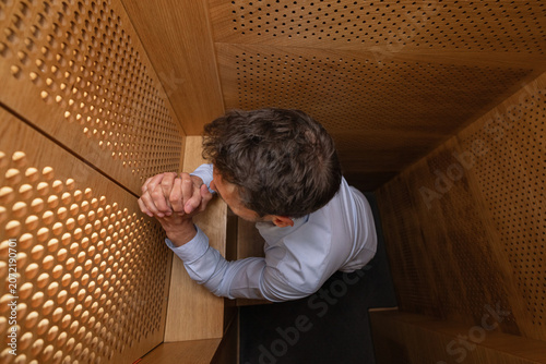 Fotografie Man penitent, in a confession booth, confessing sins to a priest to receive absolution and spiritual healing