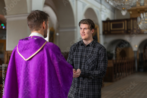 Obraz na płótnie Priest giving a holy communion, eucharistic bread to a young man from the congregation, participant in the Catholic Easter Mass