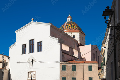 Historic Church of San Michele featuring its famous colorful patterned tiled dome against a clear blue sky in Alghero, Sardinia, Italy.