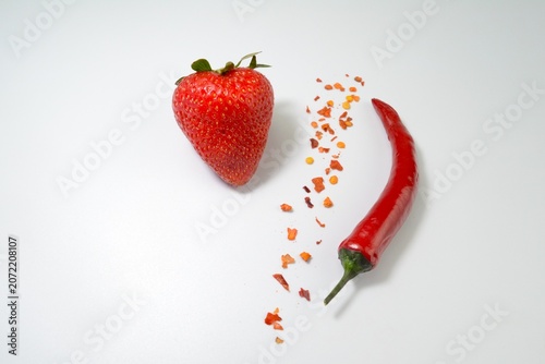 Creative food concept featuring strawberry, red chili pepper and chili flakes on white background. Sweet and spicy combination theme.