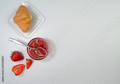 Homemade strawberry jam with croissant and fresh strawberries arranged on white background with large copy space. Breakfast concept.