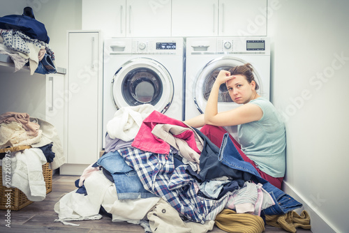 Obraz na płótnie Unhappy Stressed Woman with Pile Of Clothes Near Washing Machine in laundry room