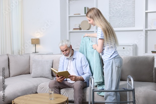 Foto Caregiver. Teenage girl taking care of elderly man indoors