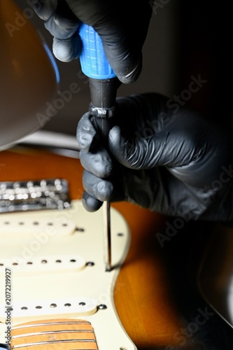 Obraz na plátně Vertical macro shot of a luthier servicing potentiometers and electronics on a sunburst stratocaster body under a lamp