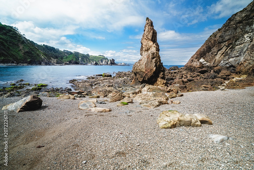Towering sea stack on pebbled beach with coastline