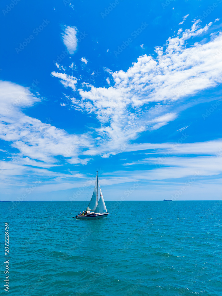 Fototapeta premium Sailing on clear blue waters under a bright sky with clouds at midday in a serene coastal area