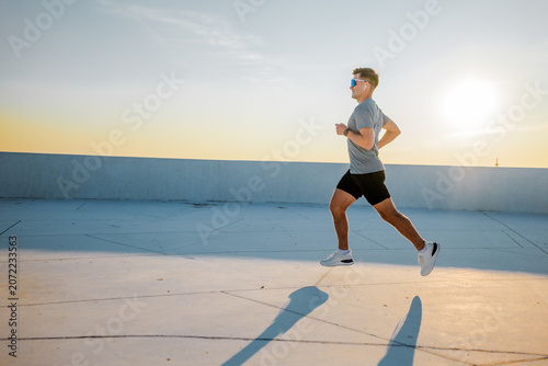 Fotografie Running at sunset, a man embraces the golden hour on a sleek rooftop, chasing dr