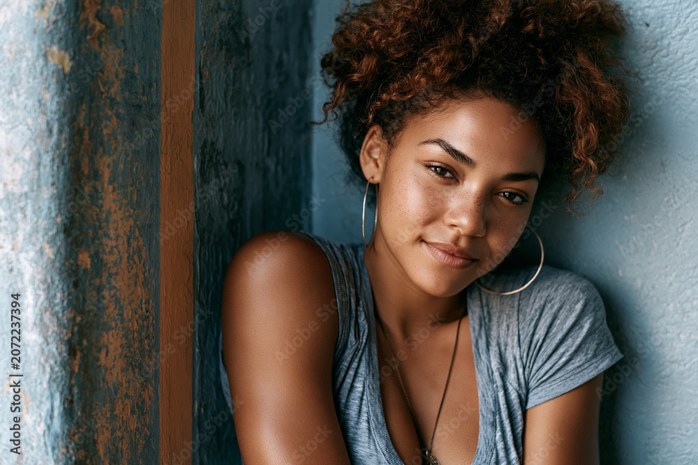 Fototapeta premium Woman leans against a wall, smiling softly in a natural light setting