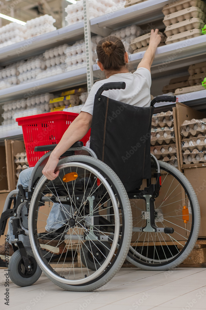 Naklejka premium A Caucasian woman in a wheelchair shopping in a supermarket.