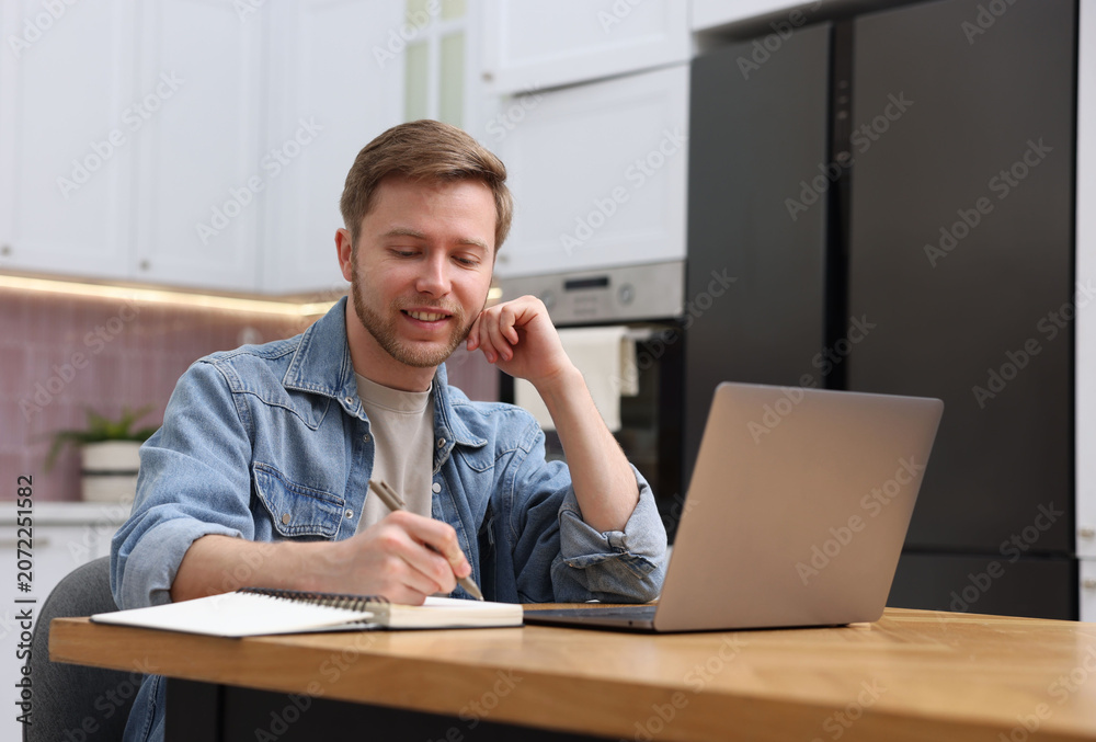 Naklejka premium Man taking notes during webinar at table indoors