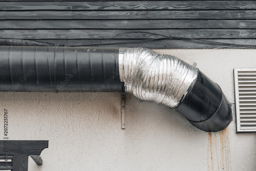 Obraz premium Exterior of an industrial building showing a black ventilation pipe connecting to a silver flexible duct on a textured wall