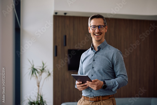 Photos Happy entrepreneur working on touchpad in office and looking at camera