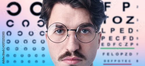 Photos Man in glasses and eye chart on color gradient background, selective focus