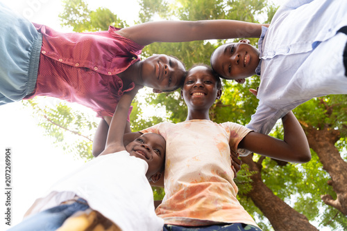 four African siblings lean in close together, creating a joyful circle of smiles, trust, and a strong sibling bond in the warm daylight.