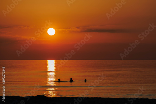 Three friends in the sea at sunset
