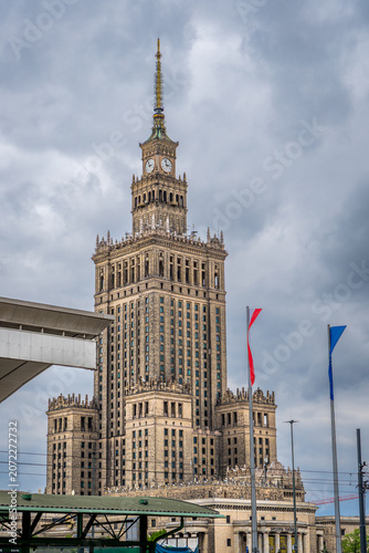 Warsaw Palace of Culture framed by green branches, ornate details under cloudy sky