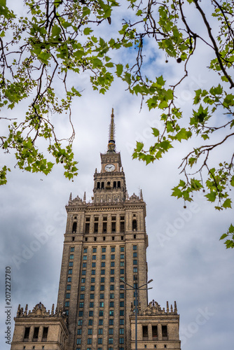 Warsaw Palace of Culture framed by green branches, ornate details under cloudy sky