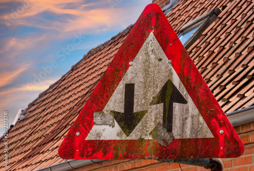 Weathered priority road sign with faded surface and moss on traditional tiled roof background under colorful evening sky