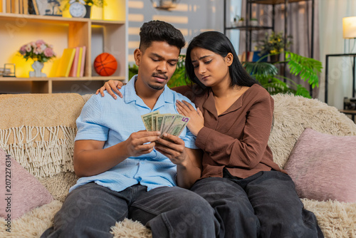 Quadro su tela Indian couple man and woman sitting on home sofa look at little cash and worry about bills and rent