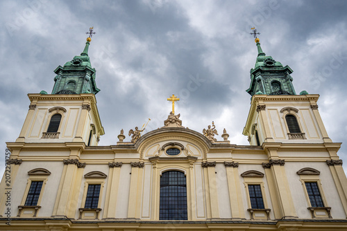 Baroque church in Warsaw with gilded cross, angels and ornate facade under dramatic spring sky