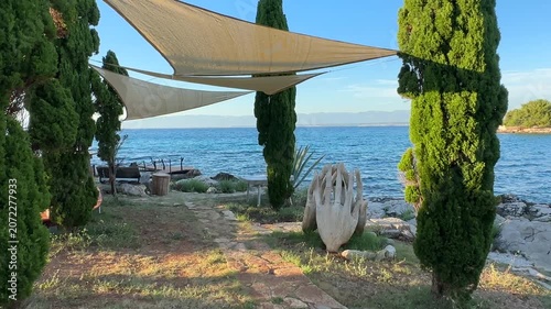 Exploring a coastal garden by the sea with shade sails and sculptures in the background