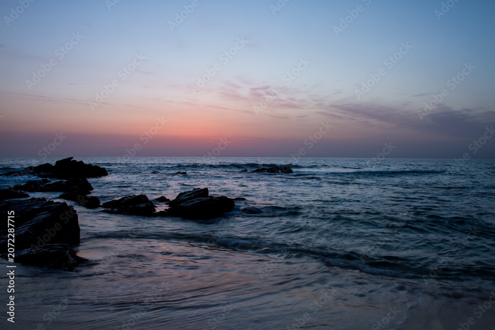 Obraz premium Serene ocean waves gently lap against dark rocks at twilight