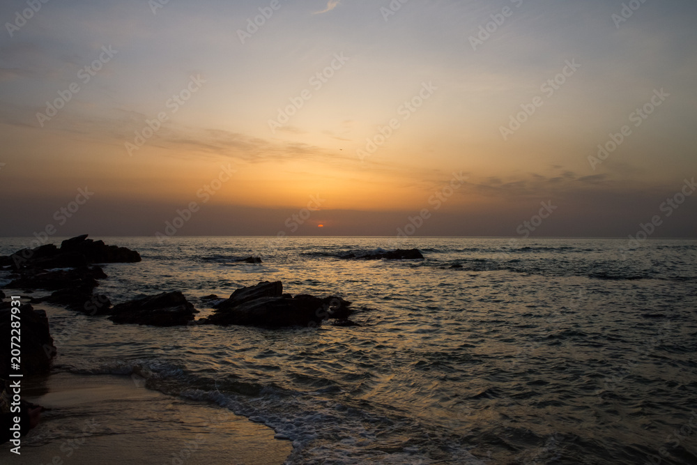 Obraz premium Stunning sunset view over calm ocean waters with rocky shoreline