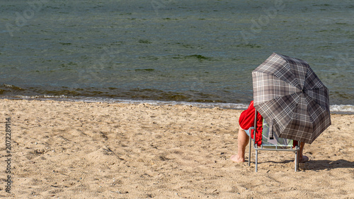 Senior man relaxing on sandy beach under umbrella by the sea