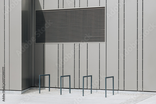 Modern white building facade with ventilation grille and bicycle racks