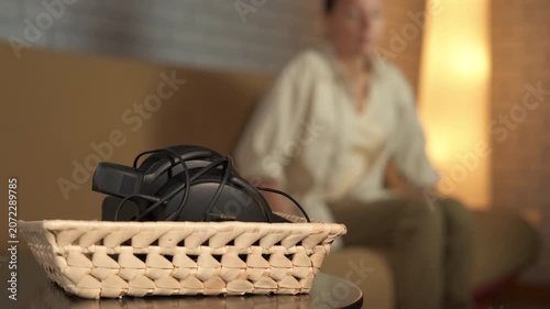 Woman grabbing headphones from basket to listen music. Relaxed woman sitting on a sofa gets up and takes her over-ear headphones from a basket on a side table, ready to enjoy some audio entertainment