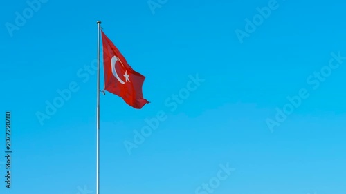 Turkish flag waving on flagpole against blue sky. Turkish national flag featuring symbolic red and white colors, crescent, and star gently waving against bright blue sky backdrop