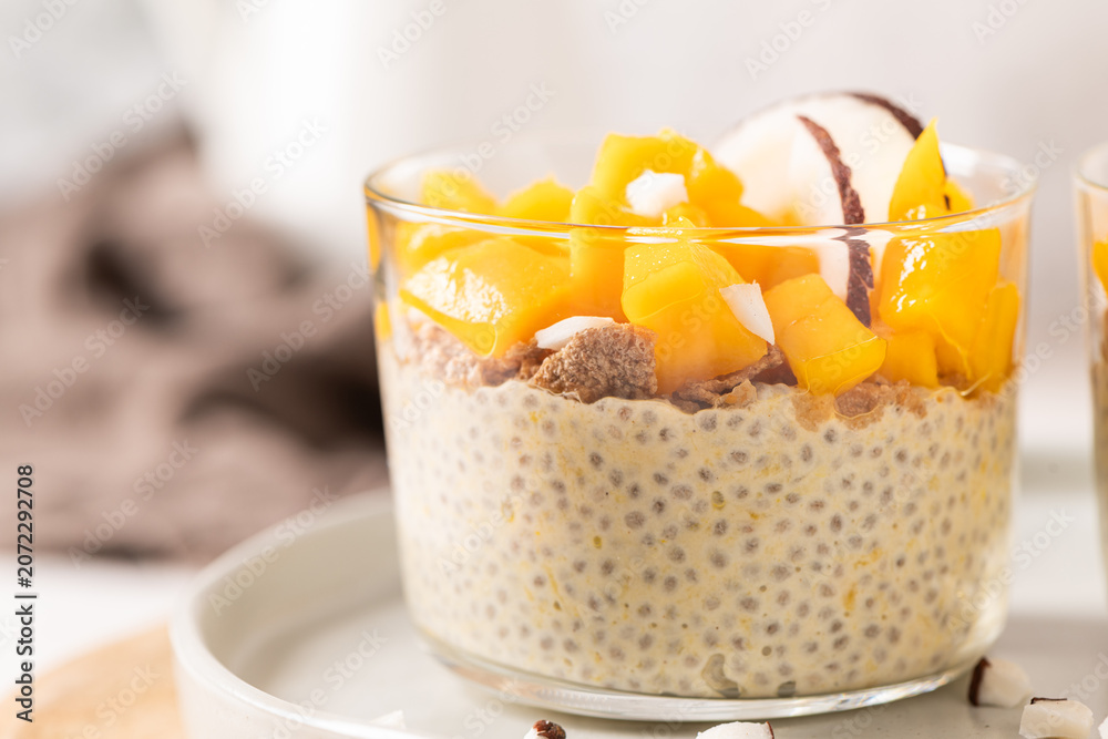 Obraz premium Creamy chia seed pudding in a glass topped with vibrant yellow mango cubes and fresh coconut slices for a healthy breakfast or tropical vegan dessert on a neutral aesthetic background with no marks
