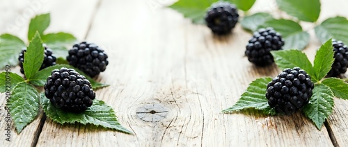 Fresh blackberries with green leaves arranged on white wooden surface, suitable for food photography, recipe blogs, and culinary design projects.