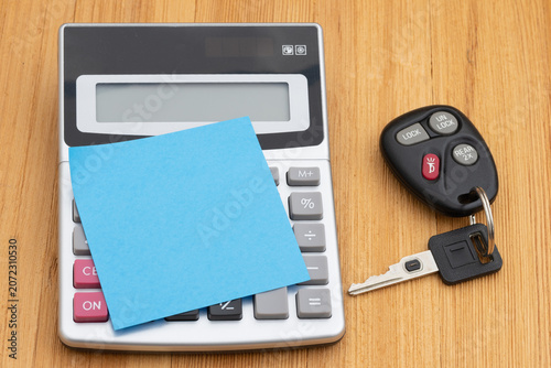 Calculator and car keys and sticky note and pen on wood desk