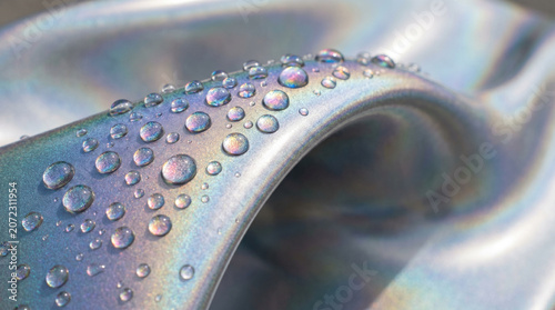 Close-up of iridescent metallic surface with water droplets, abstract texture, science background