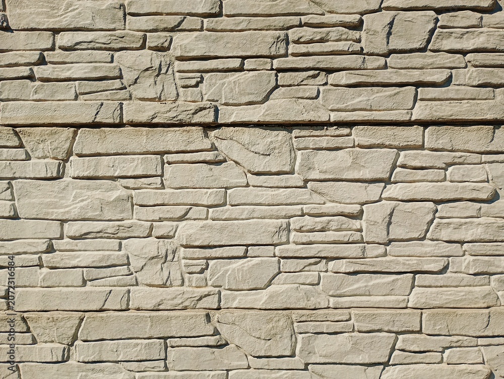 Fototapeta premium A premium textured full-frame photograph of a modern cladding wall built from rustic stacked natural stone tiles. This beautiful architectural surface showcases a rugged split-face texture in a unifor